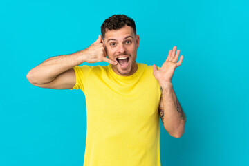 Young caucasian handsome man isolated on blue background making phone gesture and doubting