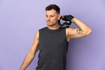 Young caucasian handsome man isolated on purple background making weightlifting with kettlebell