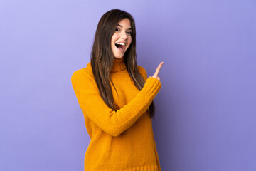 Teenager Brazilian girl over isolated purple background surprised and pointing side