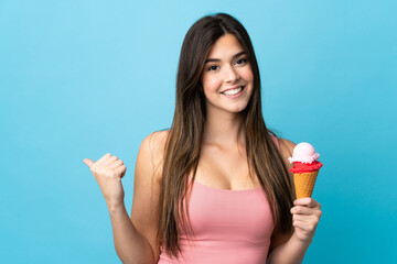 Teenager Brazilian girl holding a cornet ice cream over isolated blue background pointing to the...