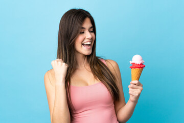 Teenager Brazilian girl holding a cornet ice cream over isolated blue background celebrating a...