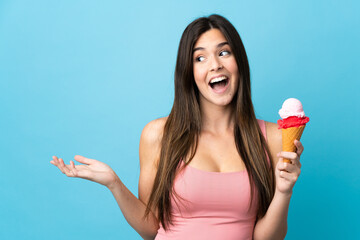Teenager Brazilian girl holding a cornet ice cream over isolated blue background with surprise...