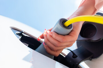 Female hands opening an electric car charging socket cap and plugging in a charger