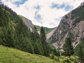 Fototapeta premium Blick mit dem Teleobjektiv zum Gramaiser Sattel mit drohenden Bergen, Wald, blauem Himmel mit Wolken in den österreichischen Alpen