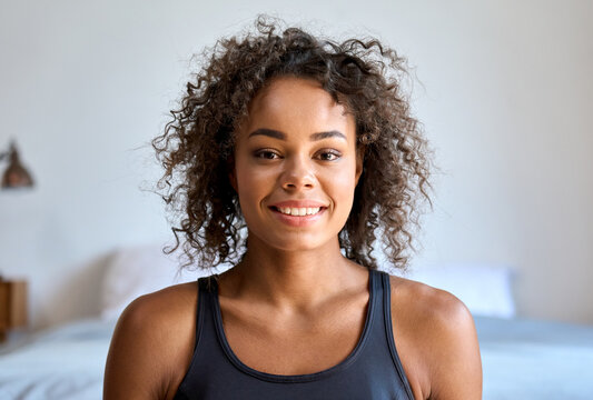 Happy smiling young attractive African American mixed race girl in sportswear posing indoors at modern bedroom apartment house looking at camera. Headshot close up portrait.