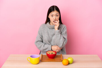Young Chinese girl  having breakfast in a table surprised and shocked while looking right