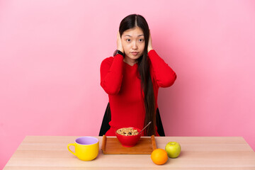 Young Chinese girl  having breakfast in a table frustrated and covering ears