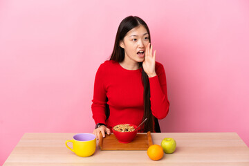 Young Chinese girl  having breakfast in a table shouting with mouth wide open to the side