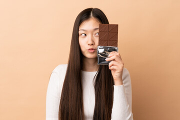 Young Chinese girl over isolated background taking a chocolate tablet and surprised