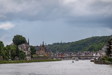 Dinant, Wallonia, Belgium - August 8, 2021: landscape just upstream of Charles de Gaulle bridge under heavy blueish cloudscape shows Meuse river, green forested hills and cityscape buildings.