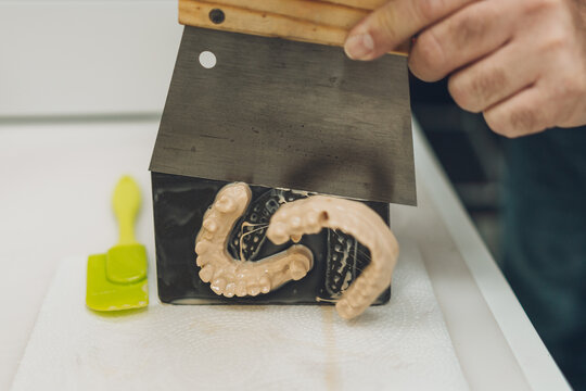 Close-up view of the hands of a man detaching a mould made with a 3D printer from the base of the printer - Powered by Adobe