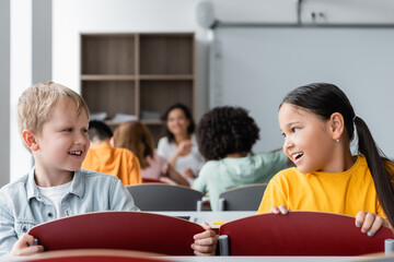 smiling interracial pupils talking during lesson in classroom