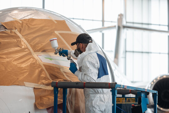 Worker painting a plane inside big hangar. Private jet maintenance and repairing job. Upgrade and check on big aircraft