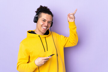 Caucasian man over isolated purple background listening music and doing guitar gesture