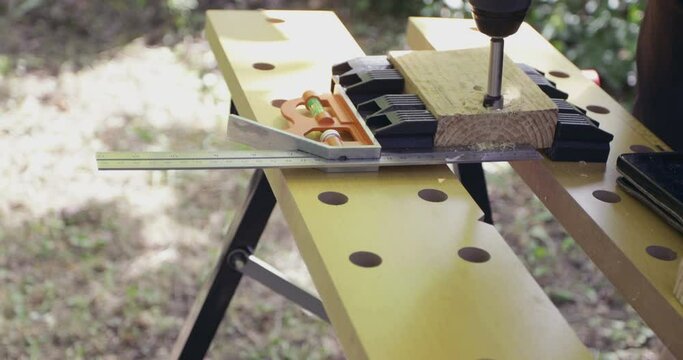 DIY woodworking, handyman drilling woodcut using cordless dril and forstner drill bit outdoors, close-up