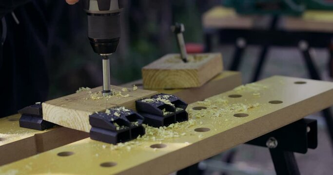DIY woodworking, handyman drilling woodcut using cordless dril and forstner drill bit outdoors, close-up