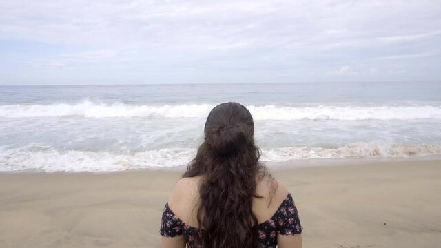 Mujer latina de espaldas contemplando el mar en la playa en Pie de la Cuesta, Acapulco, México