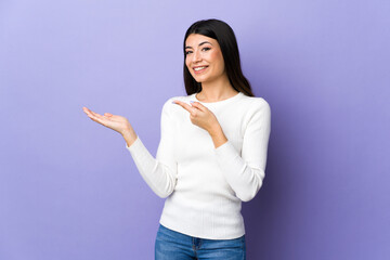 Young brunette woman over isolated purple background holding copyspace imaginary on the palm to insert an ad