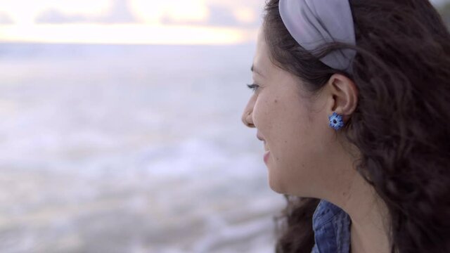 Mujer latina de perfil contempla sorprendida y sonriente el mar al atardecer en la playa en Pie de la Cuesta, Acapulco, México 