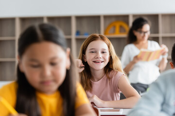 selective focus of redhead schoolgirl smiling at camera in classroom