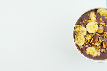 Brazilian açai in a white bowl with banana, granola and chestnuts.