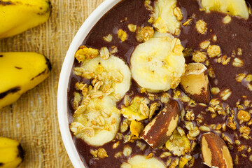 Brazilian açai in a white bowl with banana, granola and chestnuts.