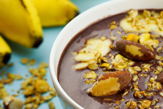 Brazilian açai in a white bowl with banana, granola and chestnuts.