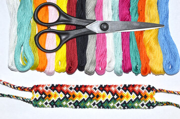 Black scissors on skeins of floss thread near woven friendship bracelet on white background