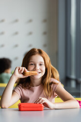 happy schoolgirl eating sandwich during lunch break at school