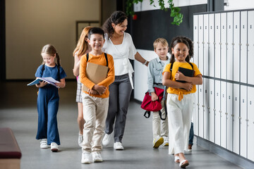 joyful kids walking in school corridor with cheerful african american teacher