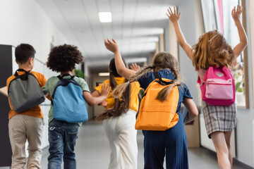 back view of multiethnic schoolkids running in school corridor