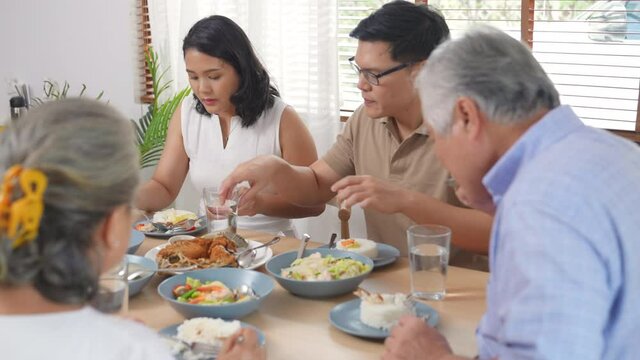Asian family having dinner together at home. Smiling adult couple with senior parents enjoy eating and sharing thai food on dining table. Happy family spending time together on weekend vacation.