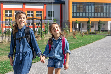 Two cheerful little girls go to school holding hands.