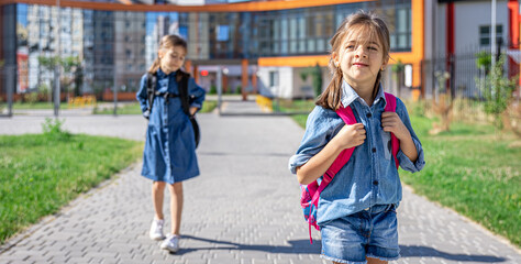 Little girls, primary school students with backpacks go from school.