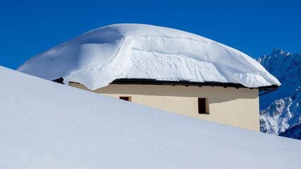 The roof of an house or hotel covered by massive quantity of fresh snow after heavy snowfall. Mountain and winter contest. Italian alps