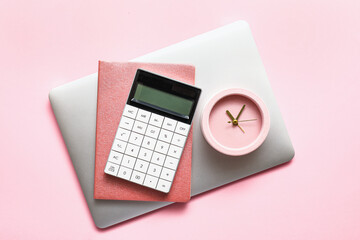 Alarm clock with calculator, notebook and laptop on color background