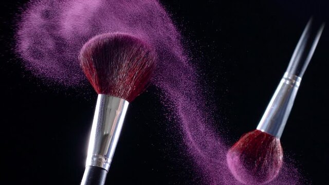 Two makeup brushes collide and cause a swirl of pink powder particles against a black background, slow motion, 300fps. 