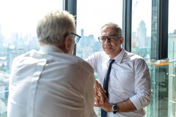 Picture of young business man taking to his older business partner. They are in white shirt and black tie. They are in a hotel lobby. 