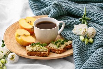 Cup of coffee with apples, sandwiches and flowers on bed
