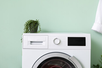 Modern washing machine with houseplant near color wall