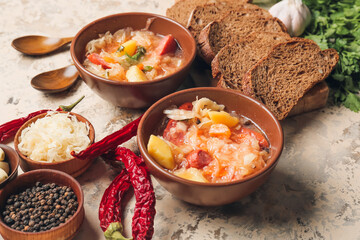 Bowls with tasty sauerkraut soup and ingredients on light background
