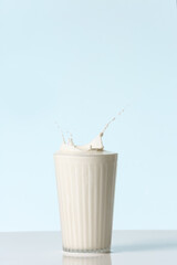 Glass of tasty milk with splashes on color background