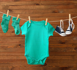 Baby clothes and shoes hanging on rope against wooden background