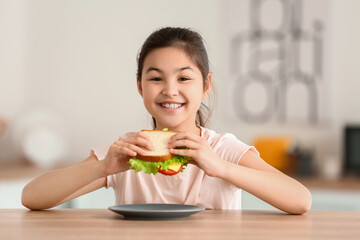 Little girl eating tasty sandwich in kitchen