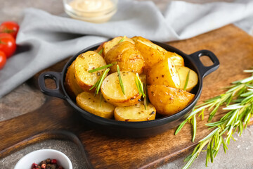 Frying pan with baked potatoes and rosemary on grey background