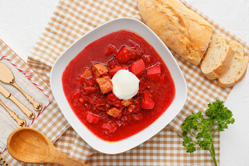 Bowl of tasty borscht with sour cream and fresh bread on light background