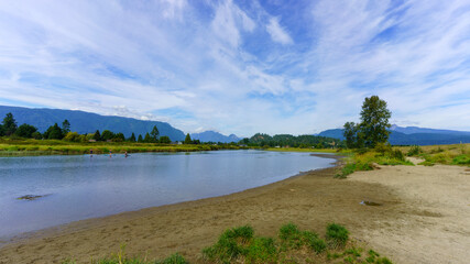 Paddleboarders on peaceful Alouette River near Pitt Meadows, BC, on a summer day with mountain backdrop.