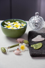 Obraz na płótnie Canvas Beautiful spa composition with plumeria flowers. Face roller and guasha massager. Facial skin care, anti age products and creme. Chinese Gua Sha massage tools.