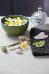 Obraz na płótnie Canvas Beautiful spa composition with plumeria flowers. Face roller and guasha massager. Facial skin care, anti age products and creme. Chinese Gua Sha massage tools.