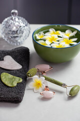 Fototapeta na wymiar Beautiful spa composition with plumeria flowers. Face roller and guasha massager. Facial skin care, anti age products and creme. Chinese Gua Sha massage tools.